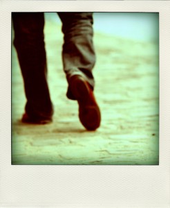 Instant photograph of lower legs and feet walking away. The subject is wearing slacks and brown shoes